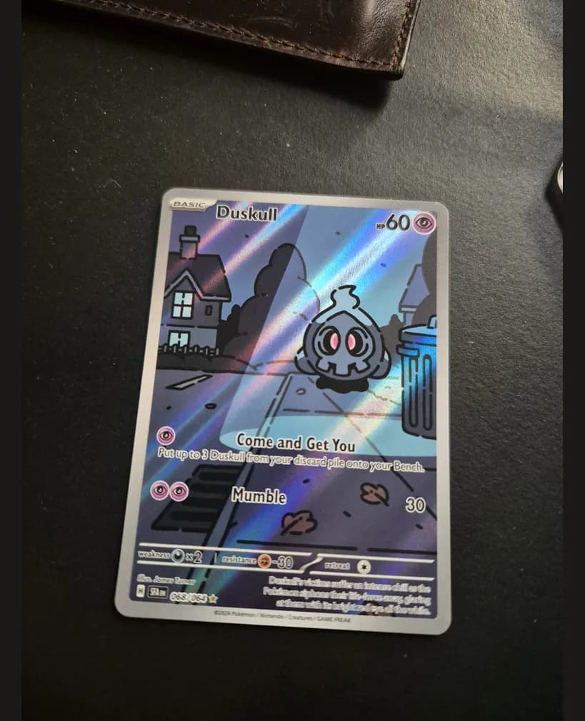 Phone photo of a Duskull Illustration Rare card taken at an angle on a desk